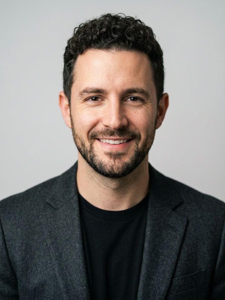 Studio headshot: the same man in a dark blazer on a gray backdrop